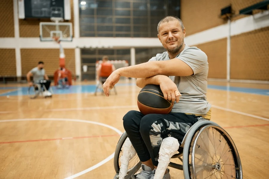 Disabled man in wheelchair holding basketball in lap and smiling at camera