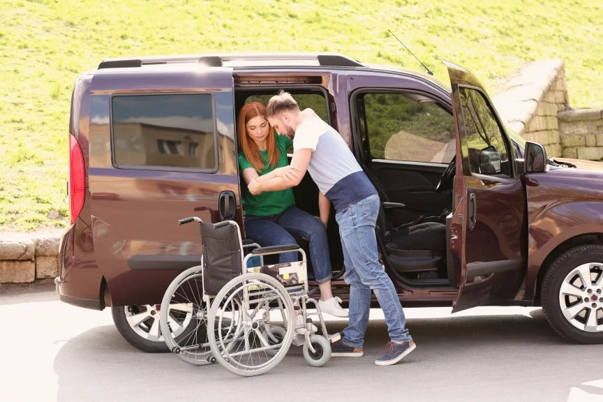 Support worker helping disabled woman to get out of van and into wheelchair