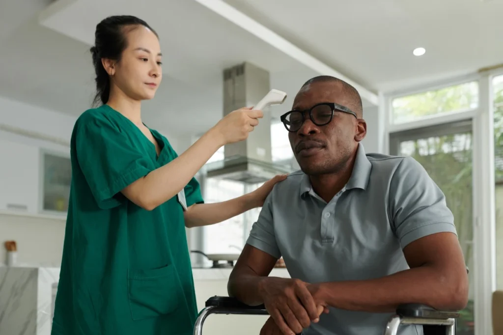Nurse taking disabled man in wheelchairs temperature at home