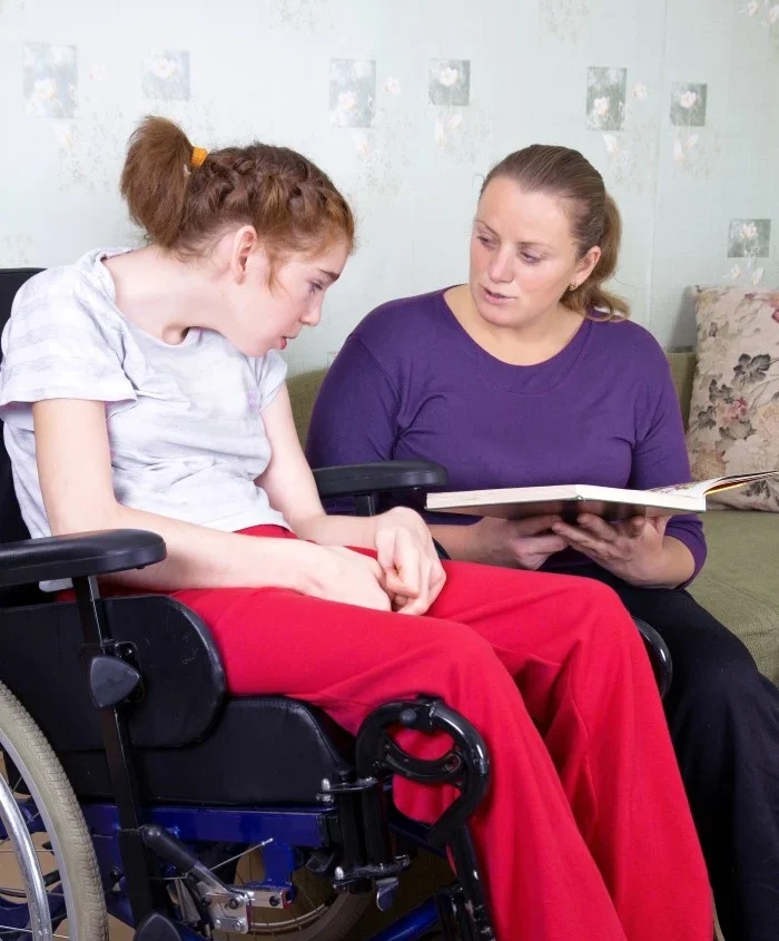 Support worker reading to highly disabled woman in wheelchair