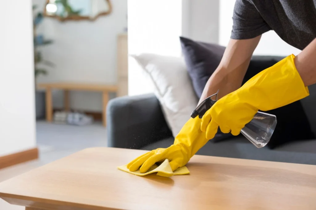 Person wearing Yellow cleaning gloves spraying and wiping down coffee table