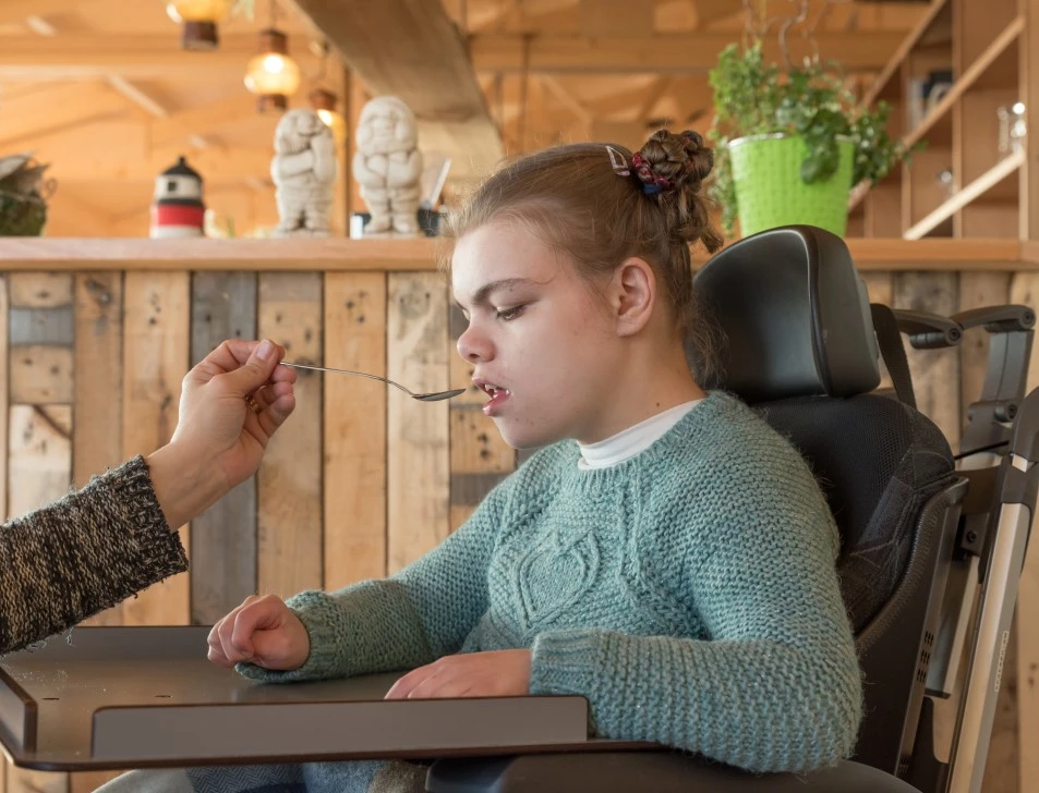 Support worker feeding highly disabled girl in wheelchair