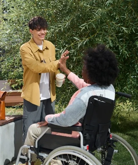 Disabled woman in wheelchair high fiving with support worker